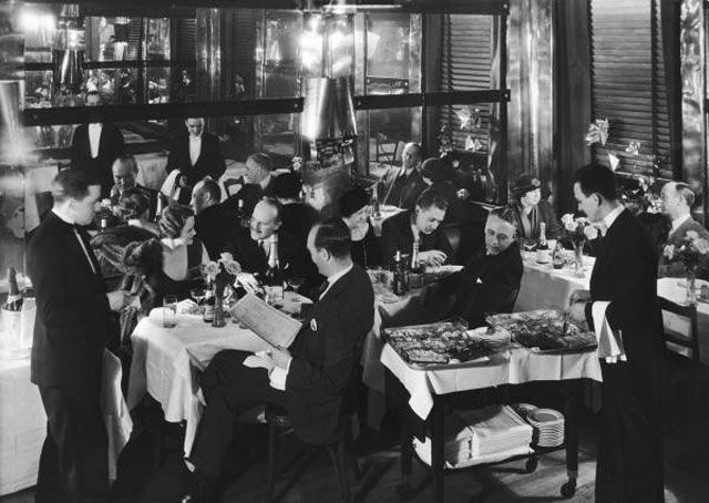 "Waiters serving food & drink to elegant patrons at the Marlborough House located on the East Side, a speakeasy haven for drinking socialites during prohibition incl. playwright Noel Coward who enjoys their Muscovite duckling."